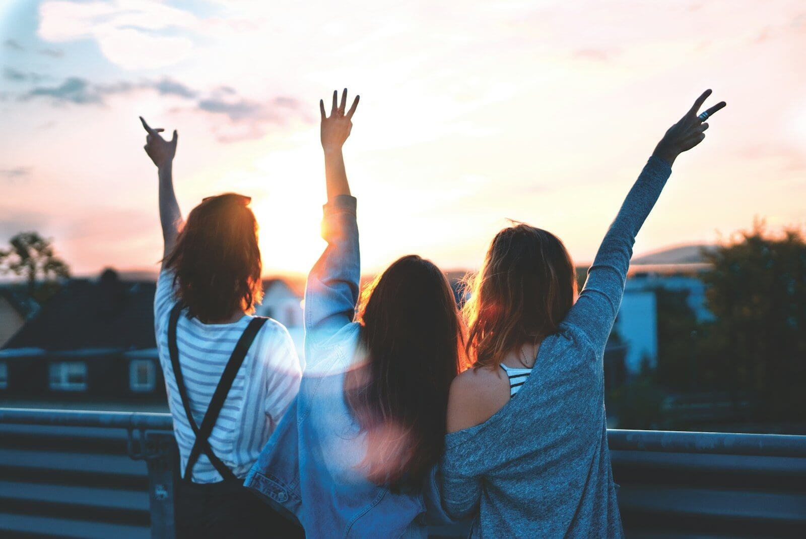 Three people with arms raised against a warm orange sky at low sun